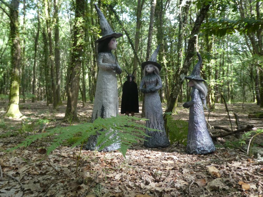 Tres figuras de brujas encapuchadas colocadas en un claro del bosque