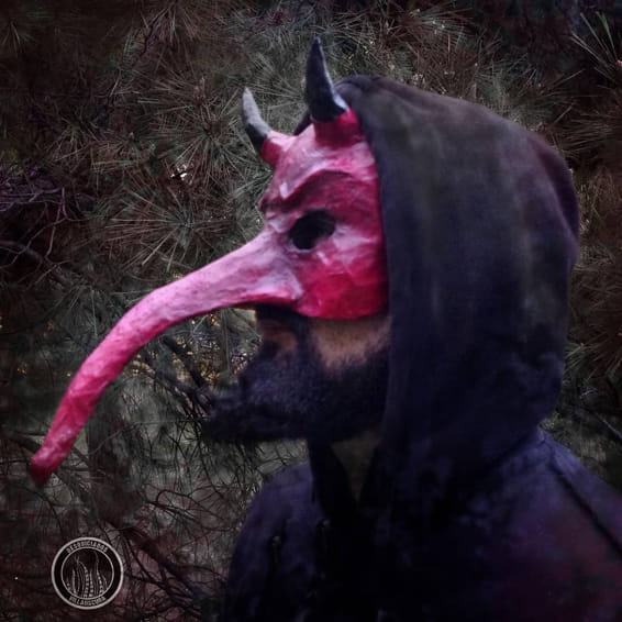 Máscara de diablo rosa con cuernos y pico largo, puesta bajo una capucha