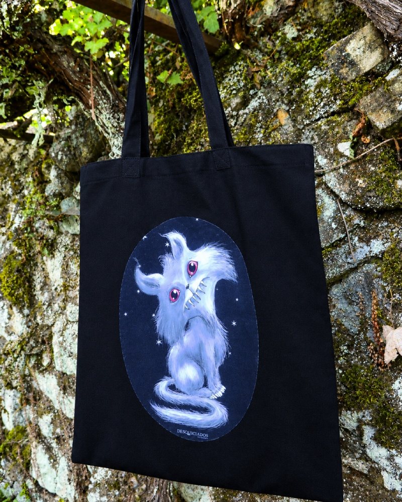 Bolsa de algodón negra con un gato blanco de ojos rosados y sonrisa dentada, dentro de un óvalo estrellado